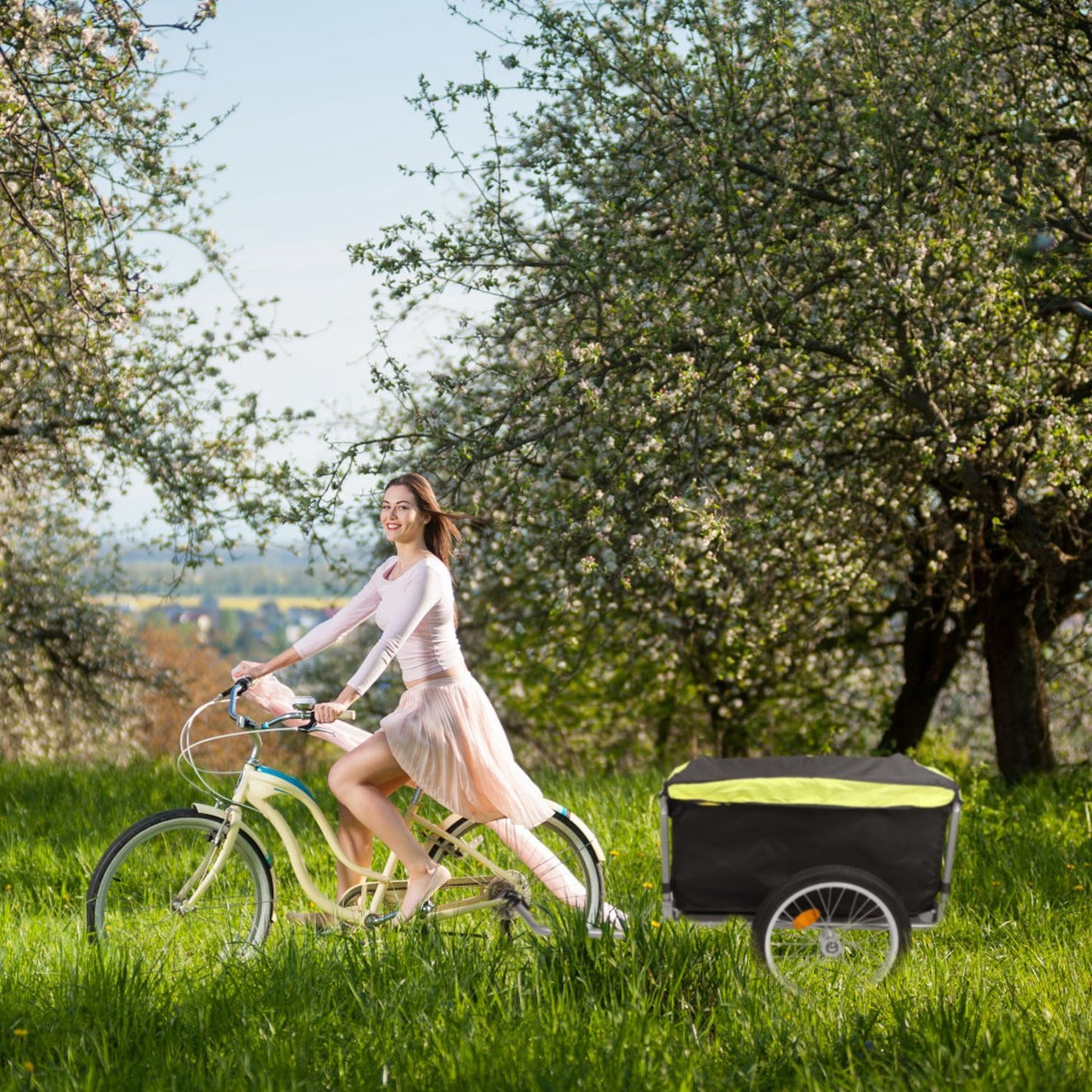 Cyclist towing closed cargo trailer through a grassy park area with trees