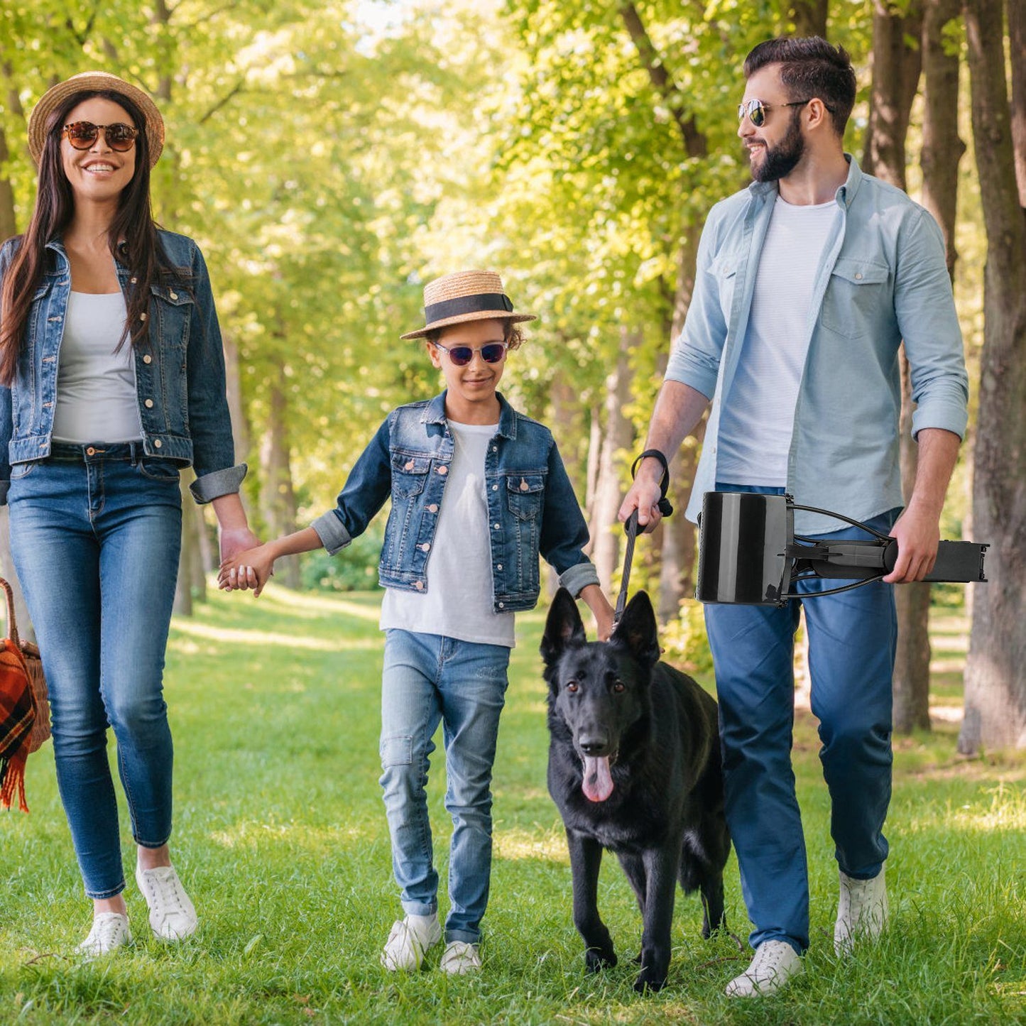 Man holding folded pooper scooper while family walks with a large black dog in a park
