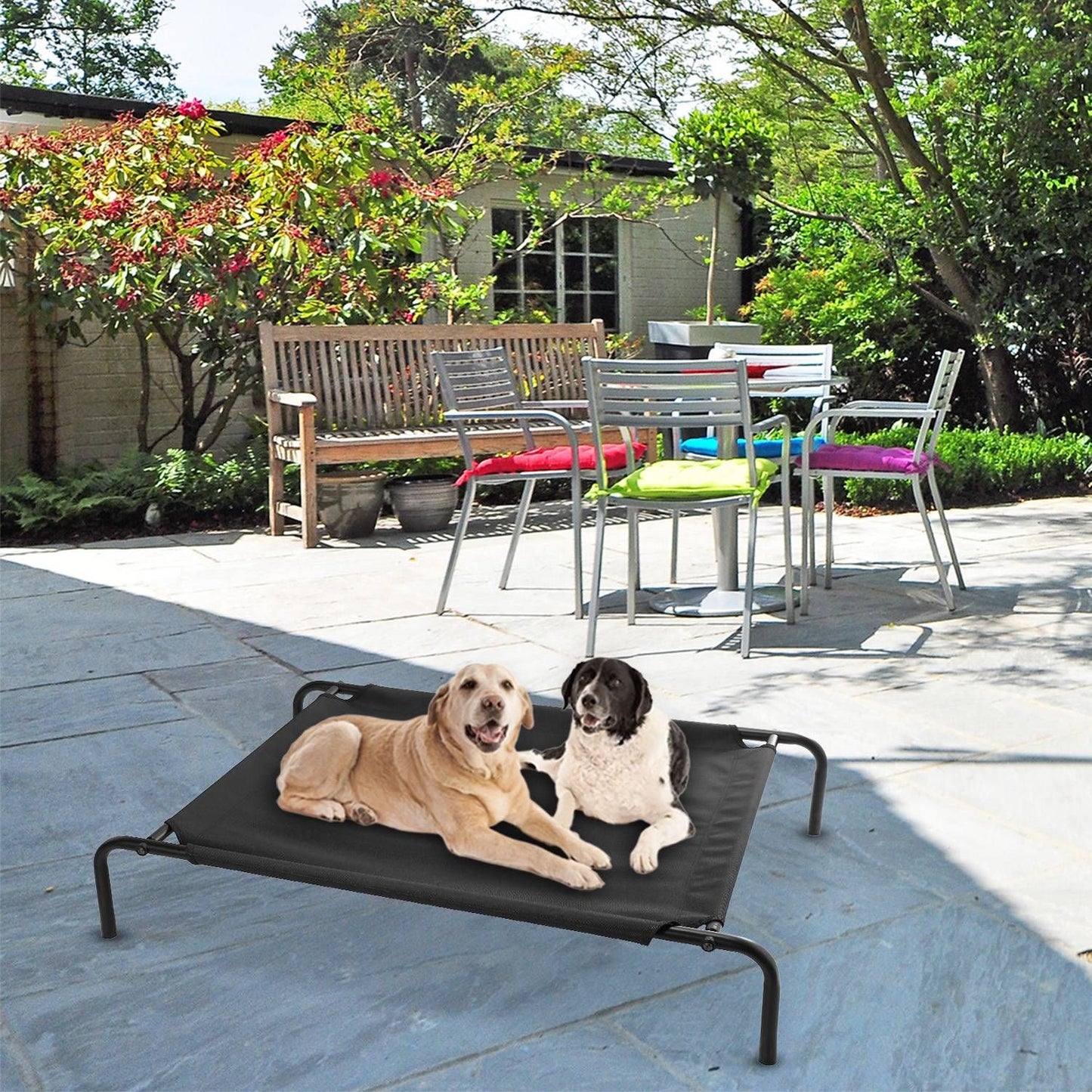 Elevated pet bed on patio pavers with two dogs resting under outdoor furniture