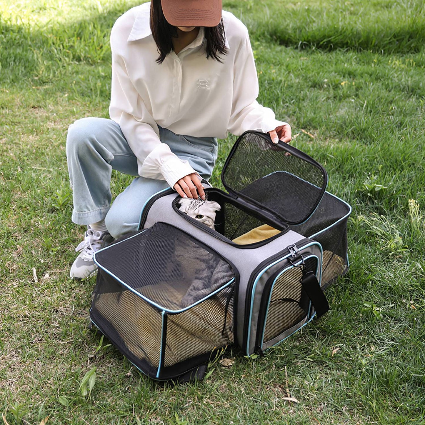 Person on grass opening the carrier top to pet a cat inside the expandable mesh carrier