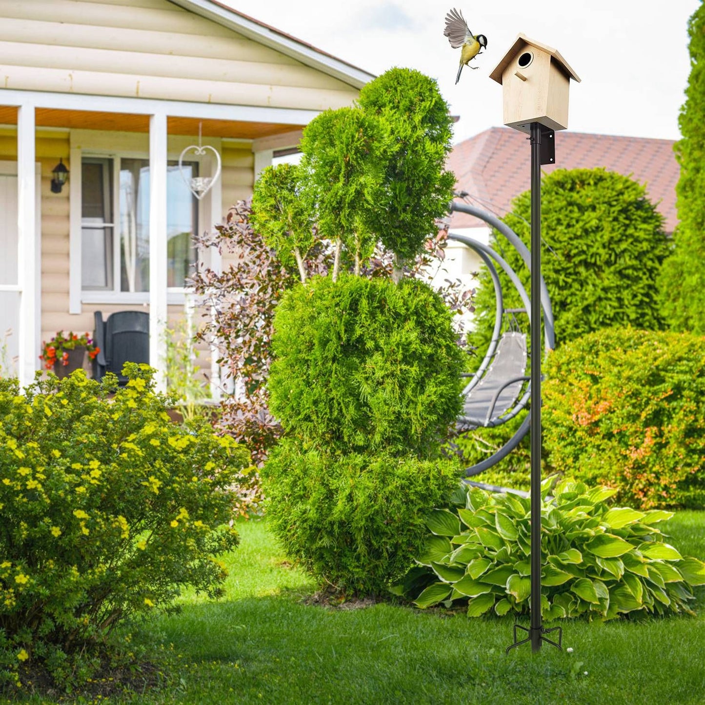 Assembled bird house pole installed in lawn next to porch, holding a small wooden birdhouse