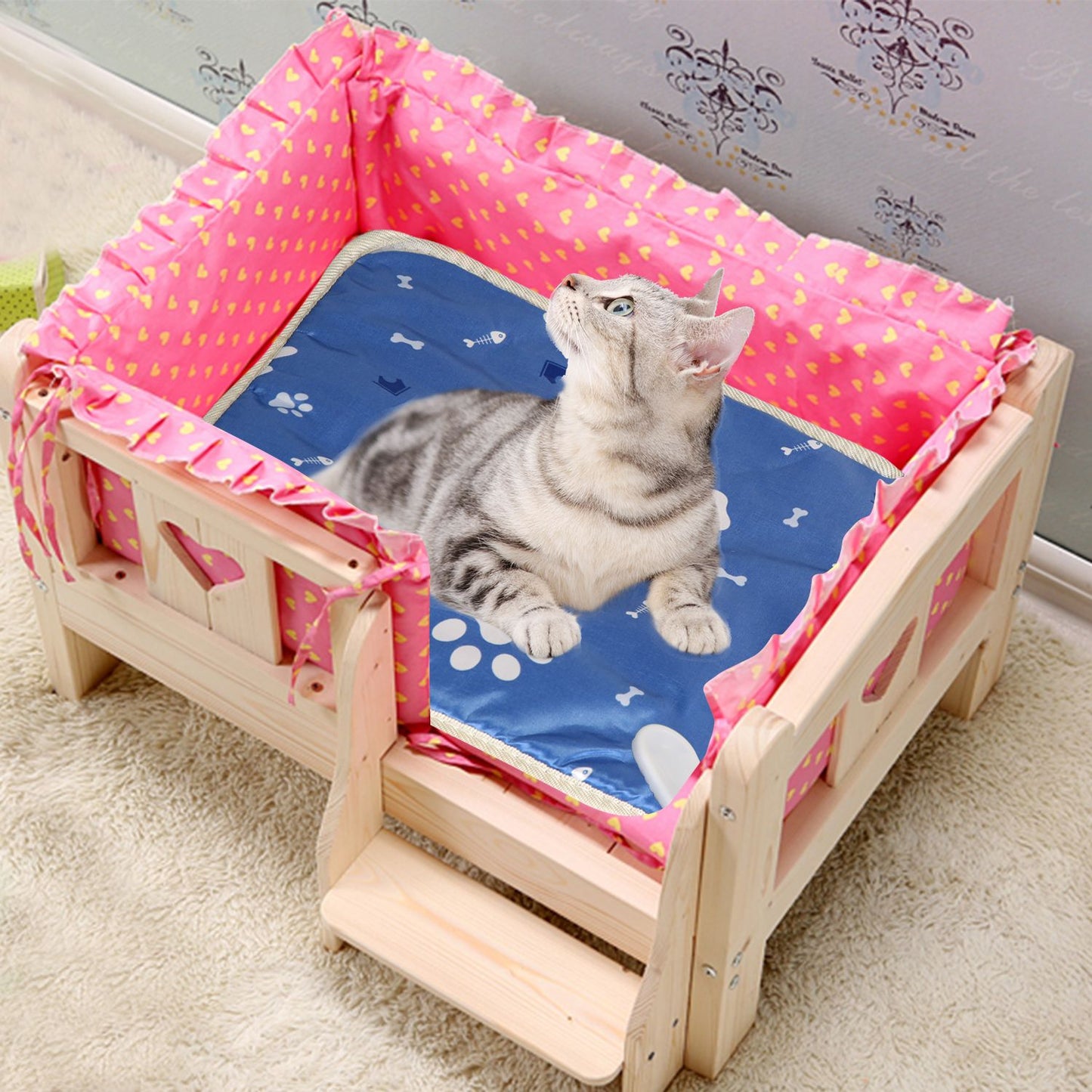 Cat resting on heated pad inside a wooden pet bed with pink lining, pad fits snugly