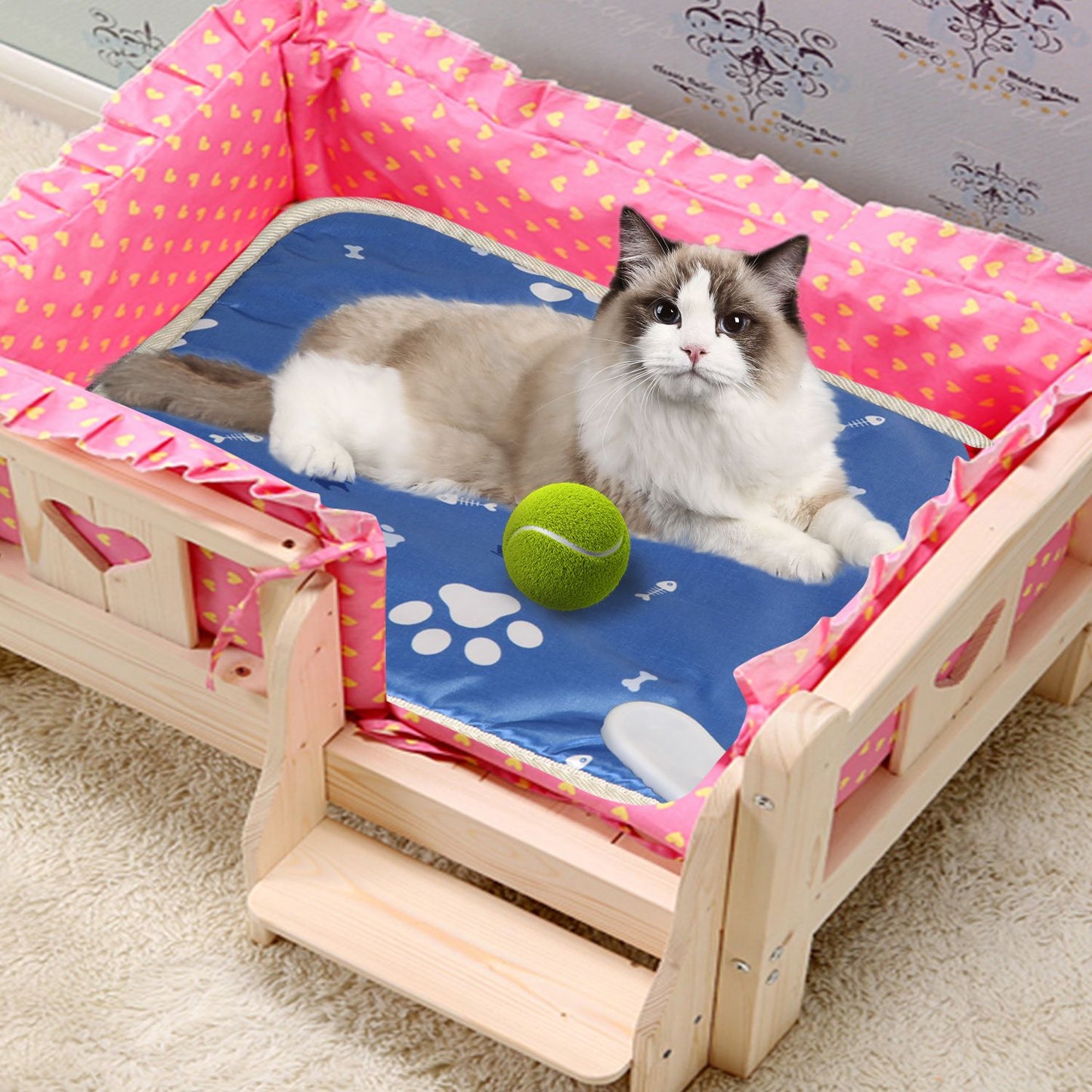 Cat lying on heated pad inside small bed with a green ball, connector visible at corner