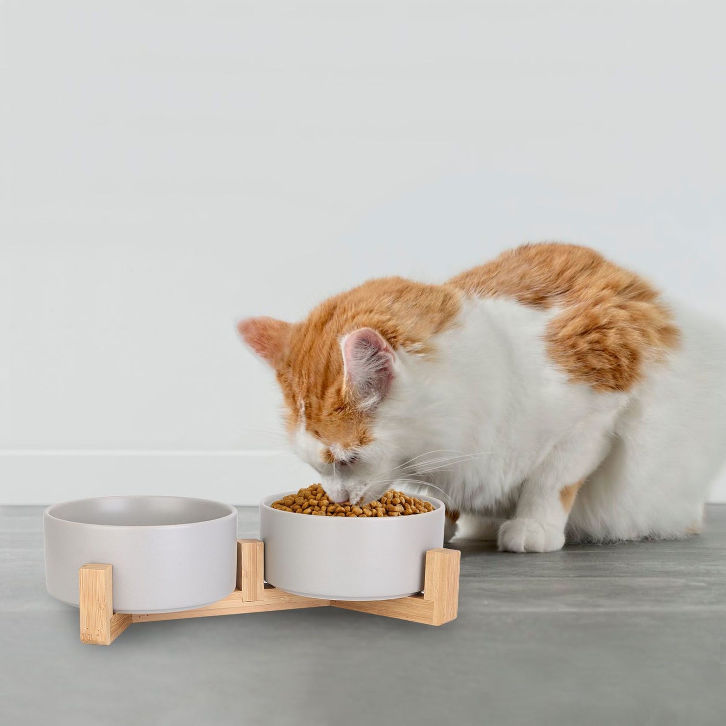 Cat feeding from one of the grey ceramic bowls in a wooden elevated stand.
