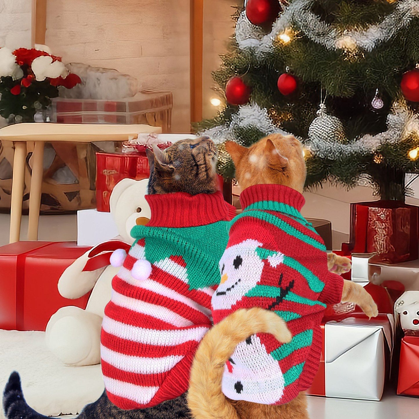 Two cats wearing red striped and snowman pet sweaters beside a Christmas tree