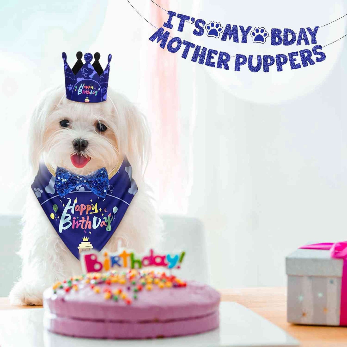 Small white dog wearing birthday bandana and crown behind a pink cake with banner overhead