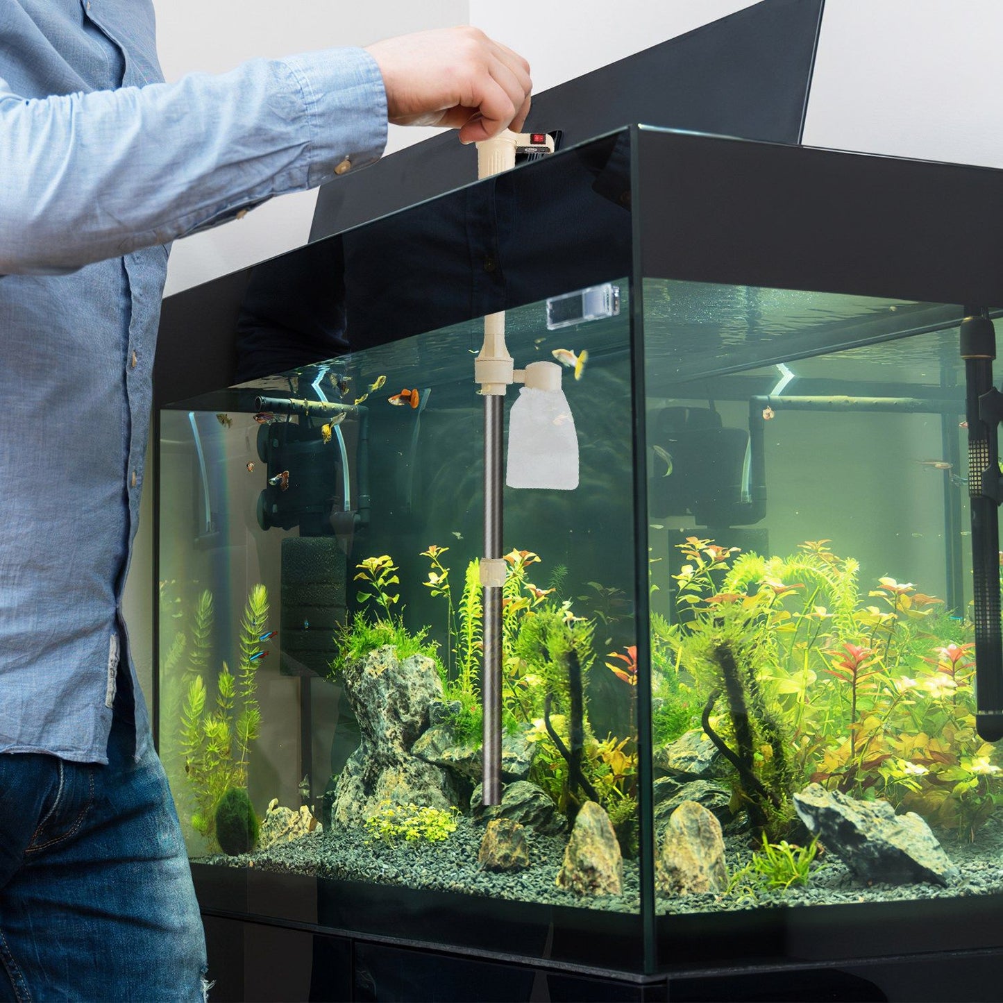 Person using the electric gravel cleaner from tank rim with tube and filter bag inside aquarium