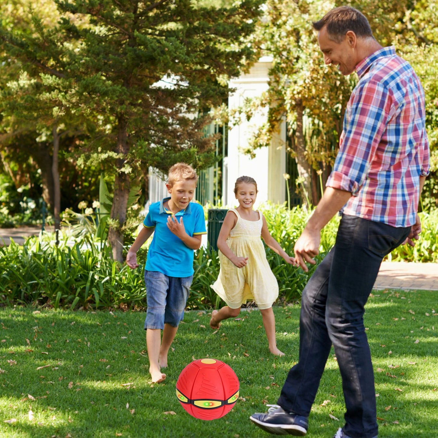 Children and adult playing outdoors with a red flying saucer ball on the grass