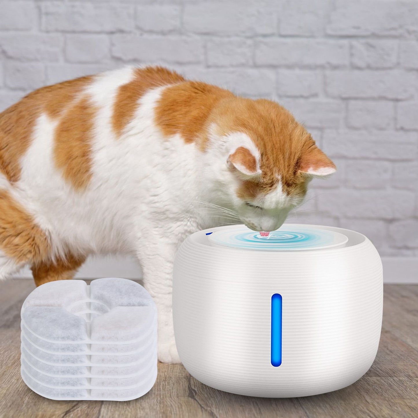 Orange-and-white cat drinking from a white automatic water fountain with spare filters stacked nearby