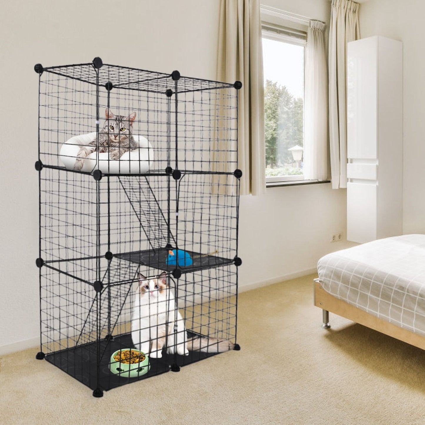 Three-tier cat cage placed in bedroom showing scale beside bed with cats inside