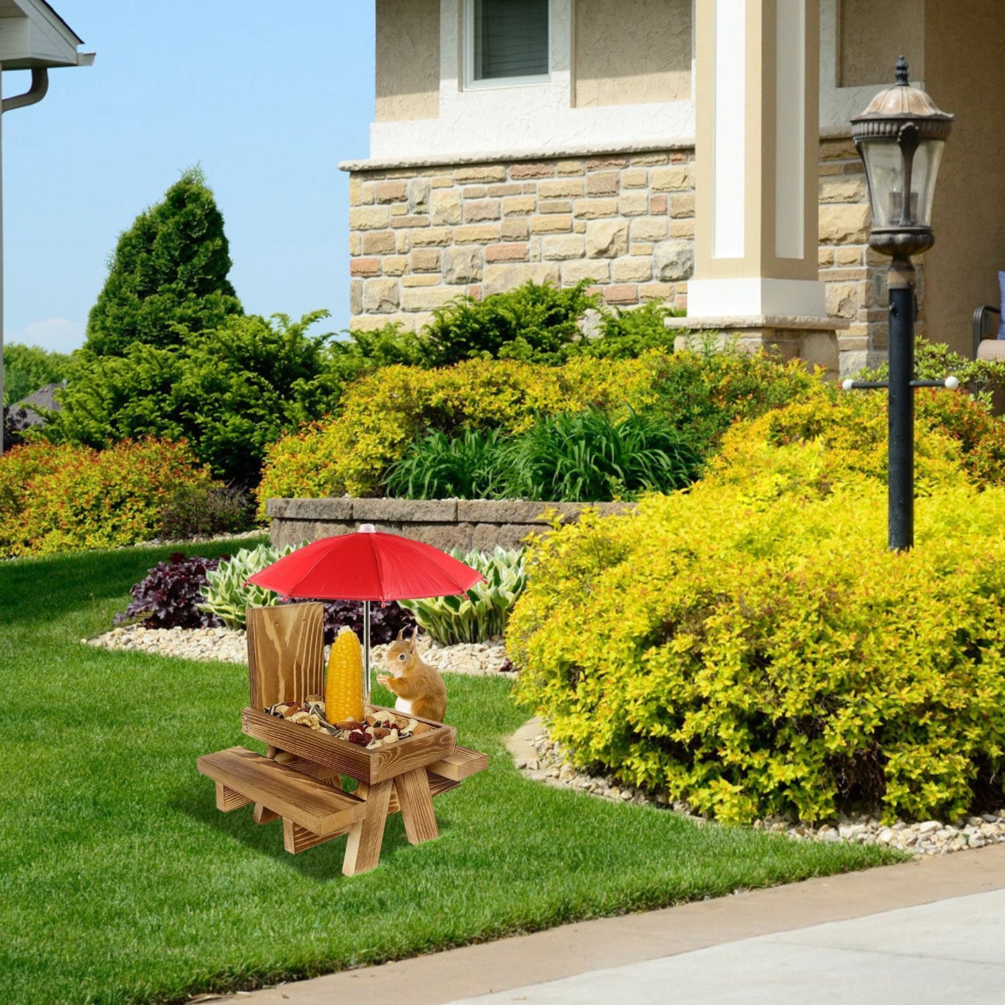 Squirrel feeder picnic table with red umbrella placed on lawn near house and shrubs