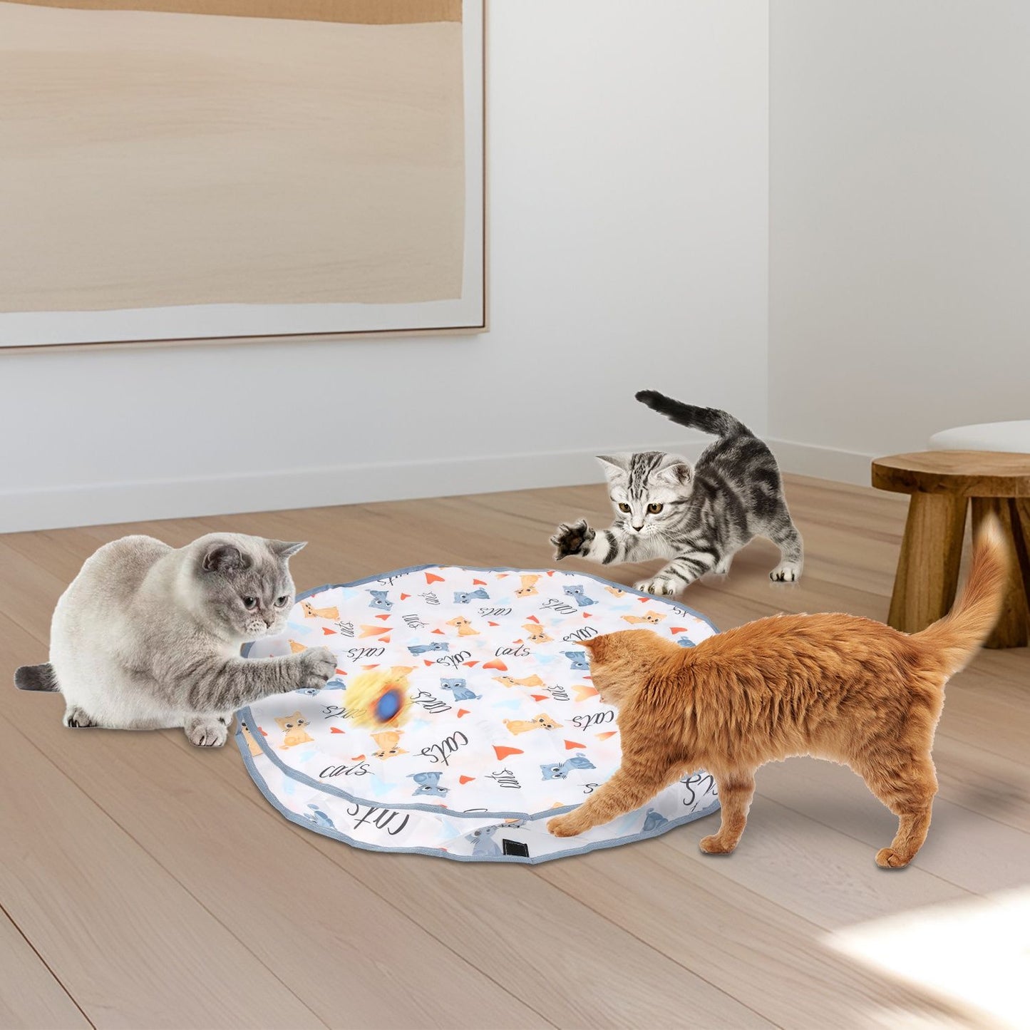 Three cats pawing a rolling toy inside a round cloth mat in a living room