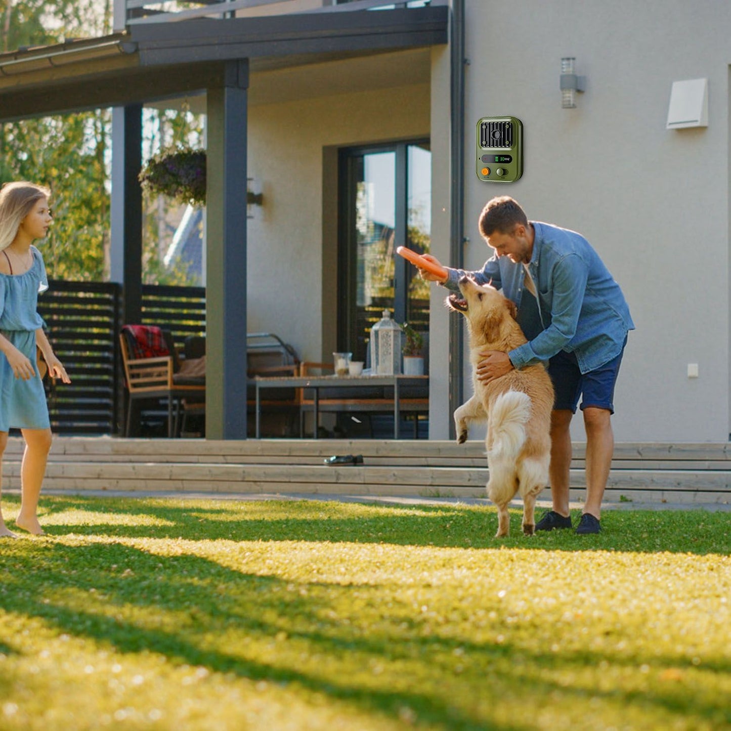 Ultrasonic device mounted on house wall while man plays fetch with dog in yard