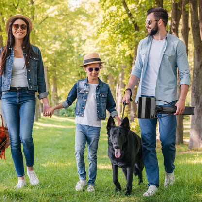Man holding folded pooper scooper while family walks with a large black dog in a park