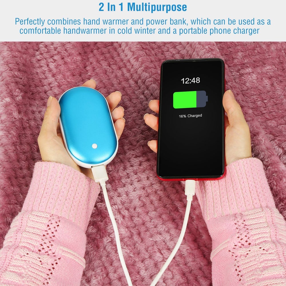 A person's hand holding a blue 2-in-1 hand warmer and portable power bank, connected to a charging smartphone displaying a low battery icon, on a soft pink knitted blanket.