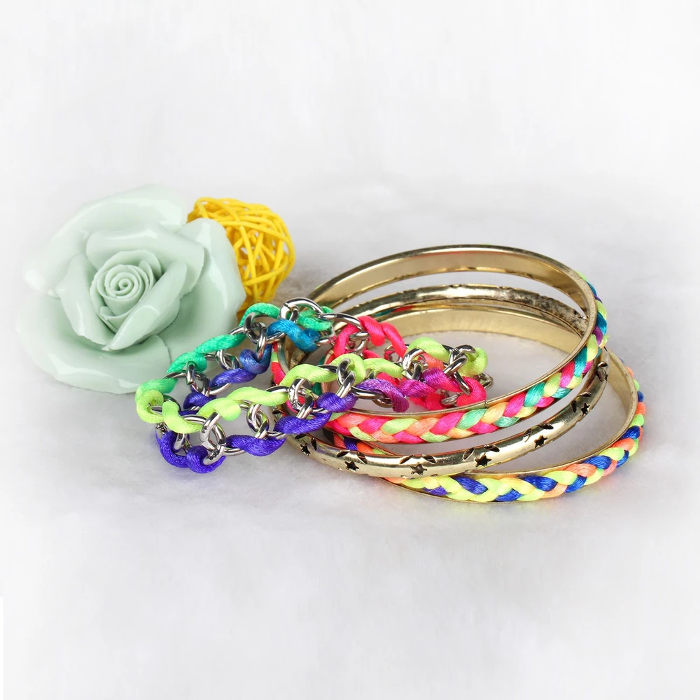 Colorful braided and metallic bangles with a decorative rose and woven orb in the background.