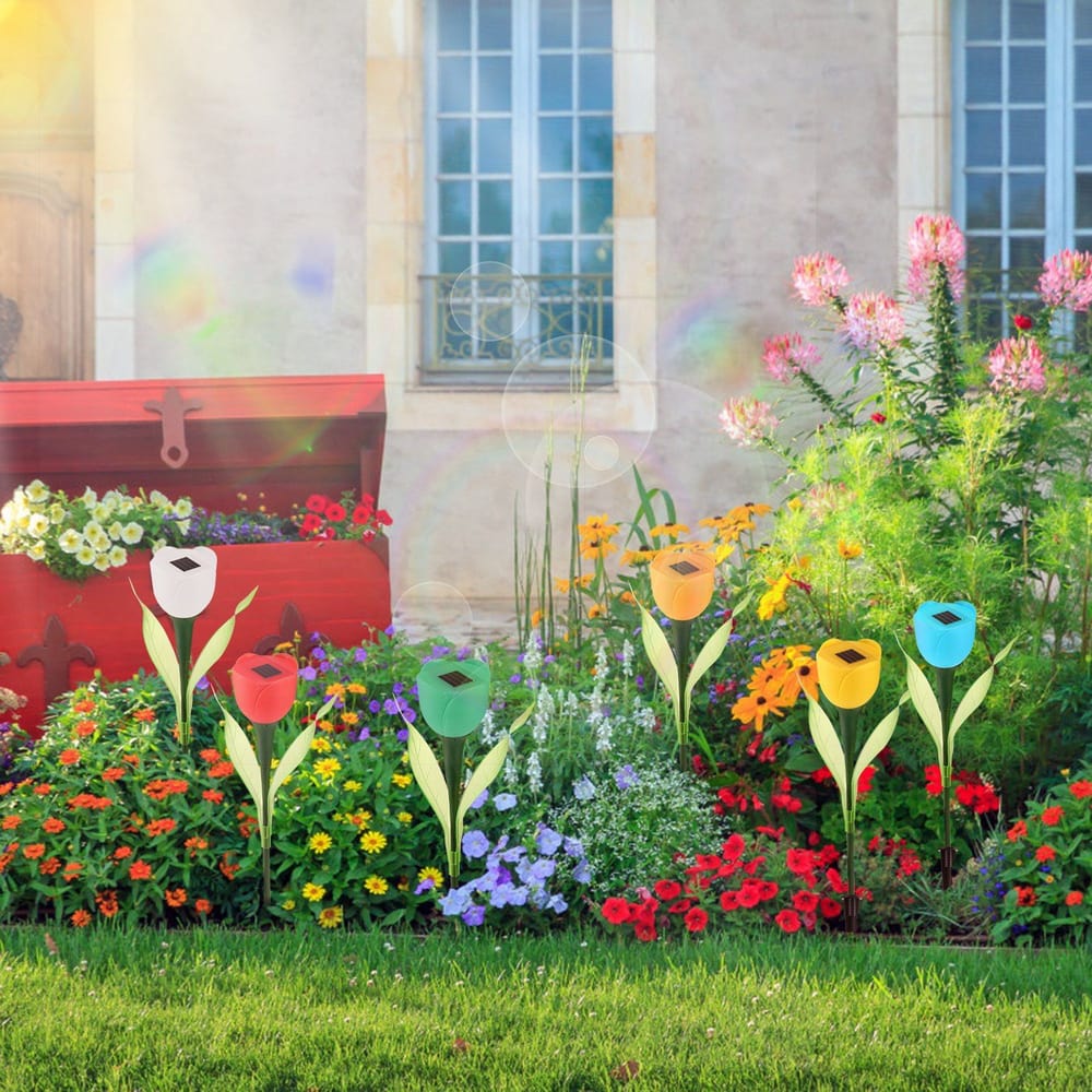 Colorful solar garden lights shaped like tulips in a vibrant flower bed with a decorative red planter in the background.