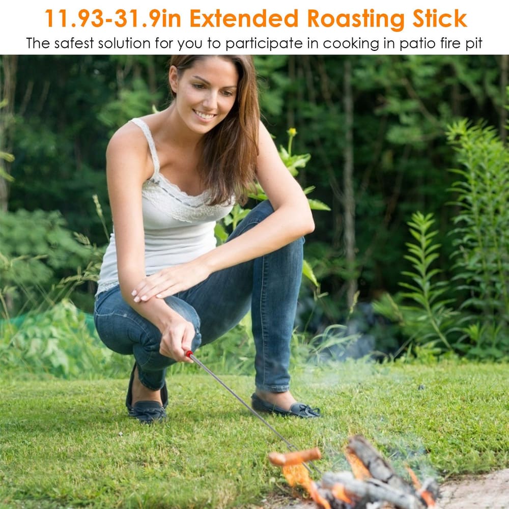 Extended roasting stick measuring 11.93-31.9 inches, demonstrating safe cooking over a patio fire pit, with a woman crouching and using the stick to tend to the flames in a green garden setting.