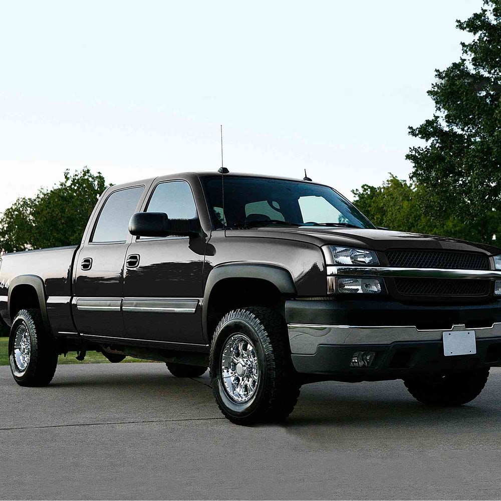 Black Chevrolet pickup truck with chrome wheels parked on pavement, surrounded by greenery.