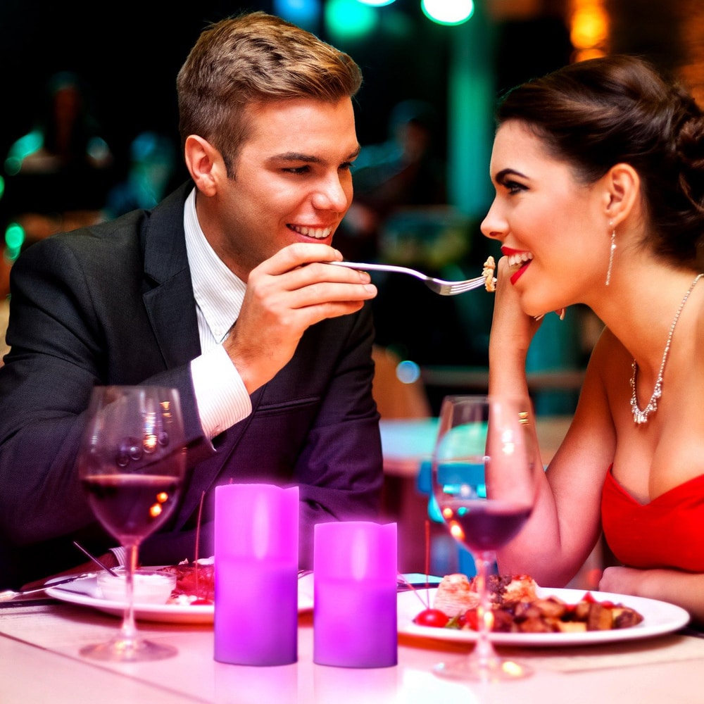 Couple enjoying a romantic dinner in a dimly lit restaurant, featuring elegant table settings, wine glasses, and purple LED candles, ideal for date night ambiance.