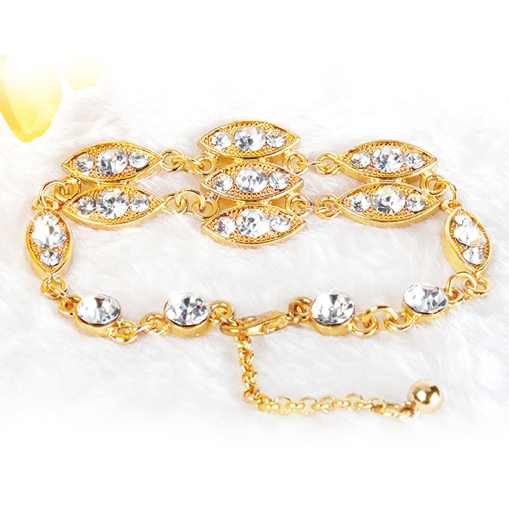 Elegant gold bracelet adorned with sparkling clear rhinestones, featuring a unique eye-shaped design, resting on a soft white surface.