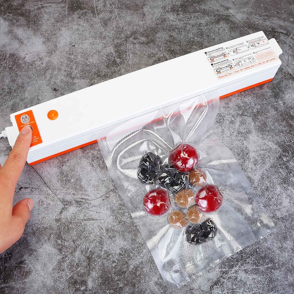 Hand using a vacuum sealer to seal a bag containing fruits and snacks on a textured gray surface.