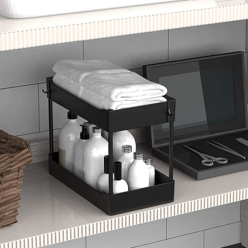Black metal bathroom storage organizer with neatly folded towels on top and various white bottles below, placed on a modern vanity countertop with a basket and grooming tools.
