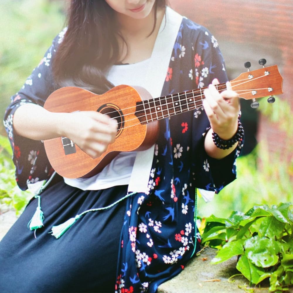 Young woman playing a ukulele outdoors, wearing a floral kimono and a black skirt, surrounded by greenery.
