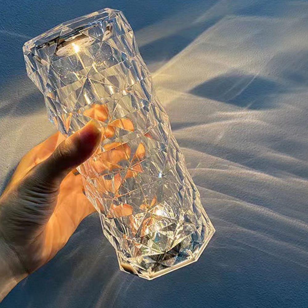 Hand holding a crystal clear geometric lantern casting reflections, showcasing its modern design and warm light.