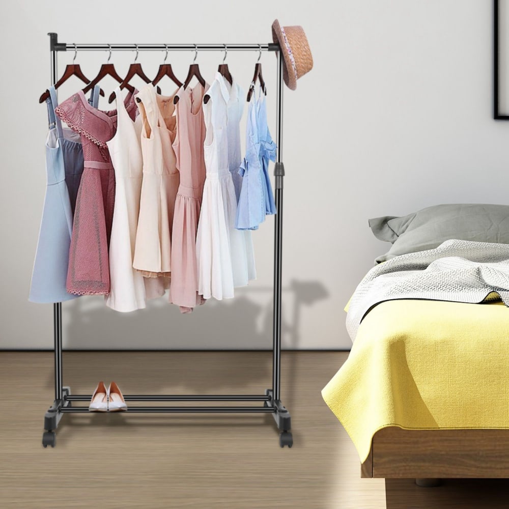 Clothing rack displaying a variety of pastel dresses in shades of blue, pink, and white, with a stylish straw hat on top, set in a contemporary bedroom with a neatly made bed and soft yellow blanket.