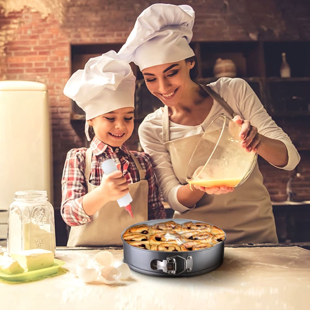 A mother and child in matching chef hats prepare a delicious cinnamon roll cake in a modern kitchen, featuring a springform pan filled with baked goods, surrounded by baking ingredients like eggs and flour.