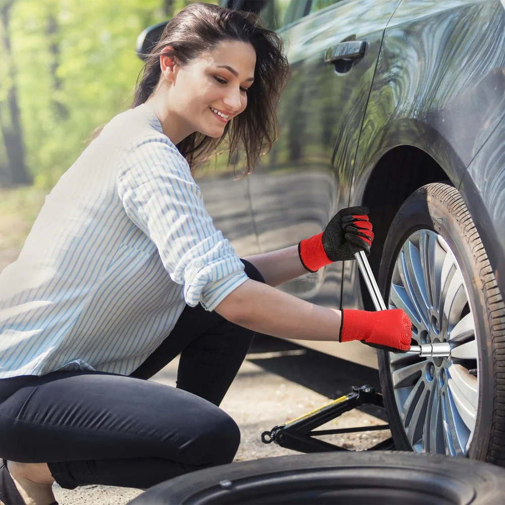 A woman in red gloves uses a wrench to change a tire on a car in a forested outdoor setting.