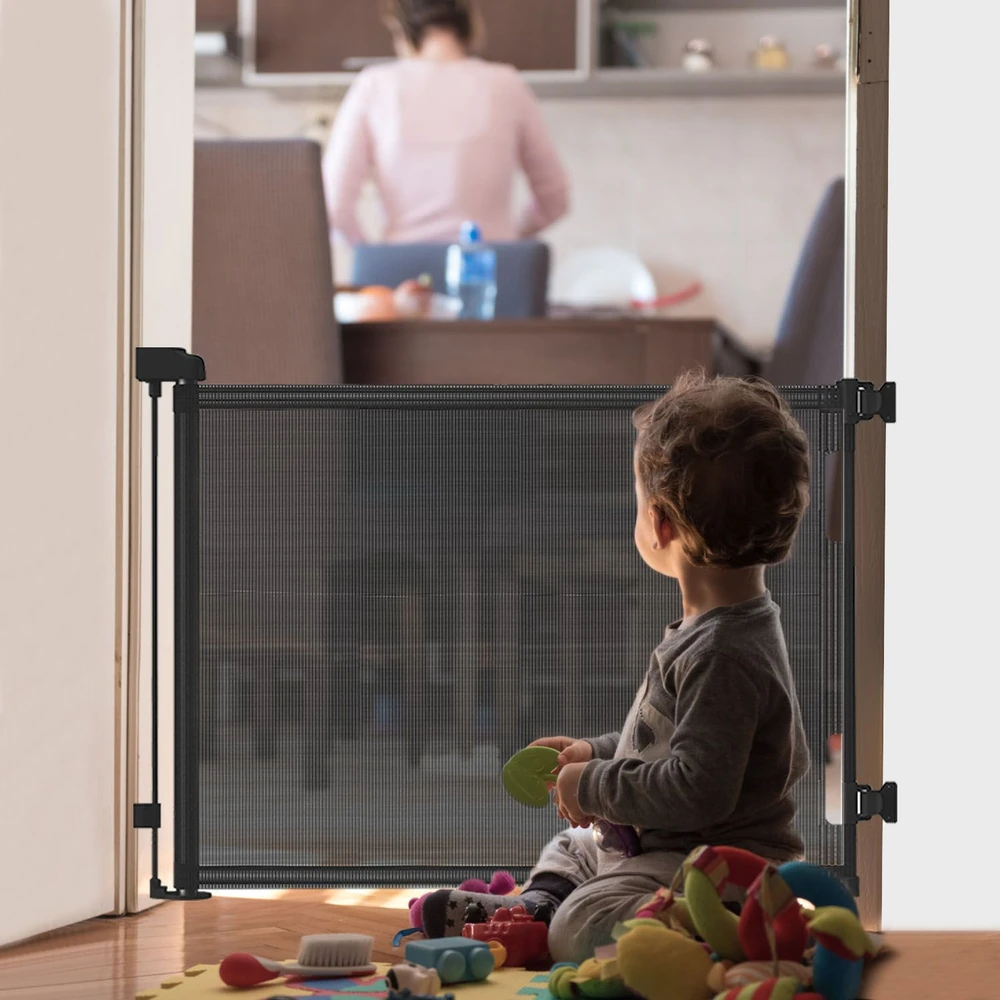 Baby safety gate in an indoor setting with a young child sitting on the floor surrounded by toys, watching a parent in the background.