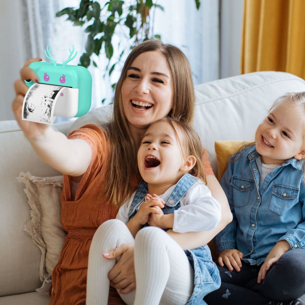 A mother holding a fun instant photo printer while taking a selfie with two kids, enjoying a cozy moment on a sofa in a bright living room.