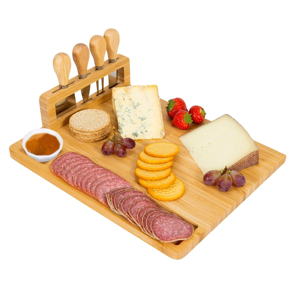 Bamboo charcuterie board featuring assorted cheeses, cured meats, crackers, fresh strawberries, and grapes, with a set of cheese tools displayed on top.