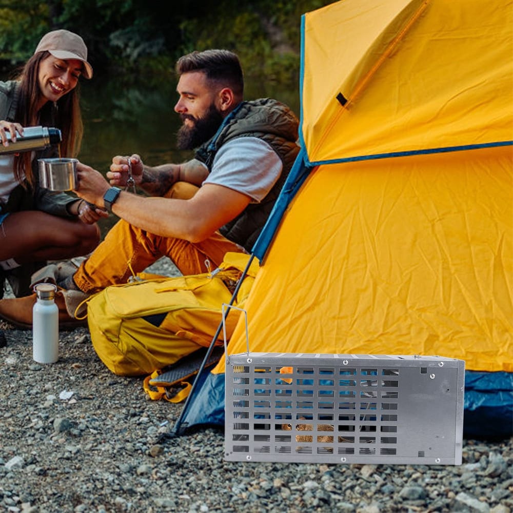 Stainless steel portable campfire grill being used by friends enjoying a camping trip near a bright yellow tent by a river.
