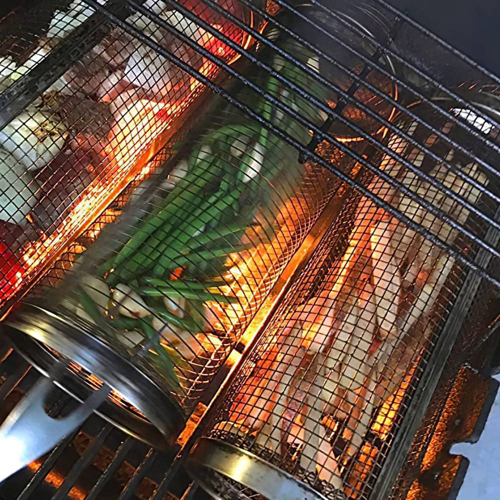 Grilling colorful vegetables, including green onions and assorted meats, in a commercial grill basket over glowing embers.
