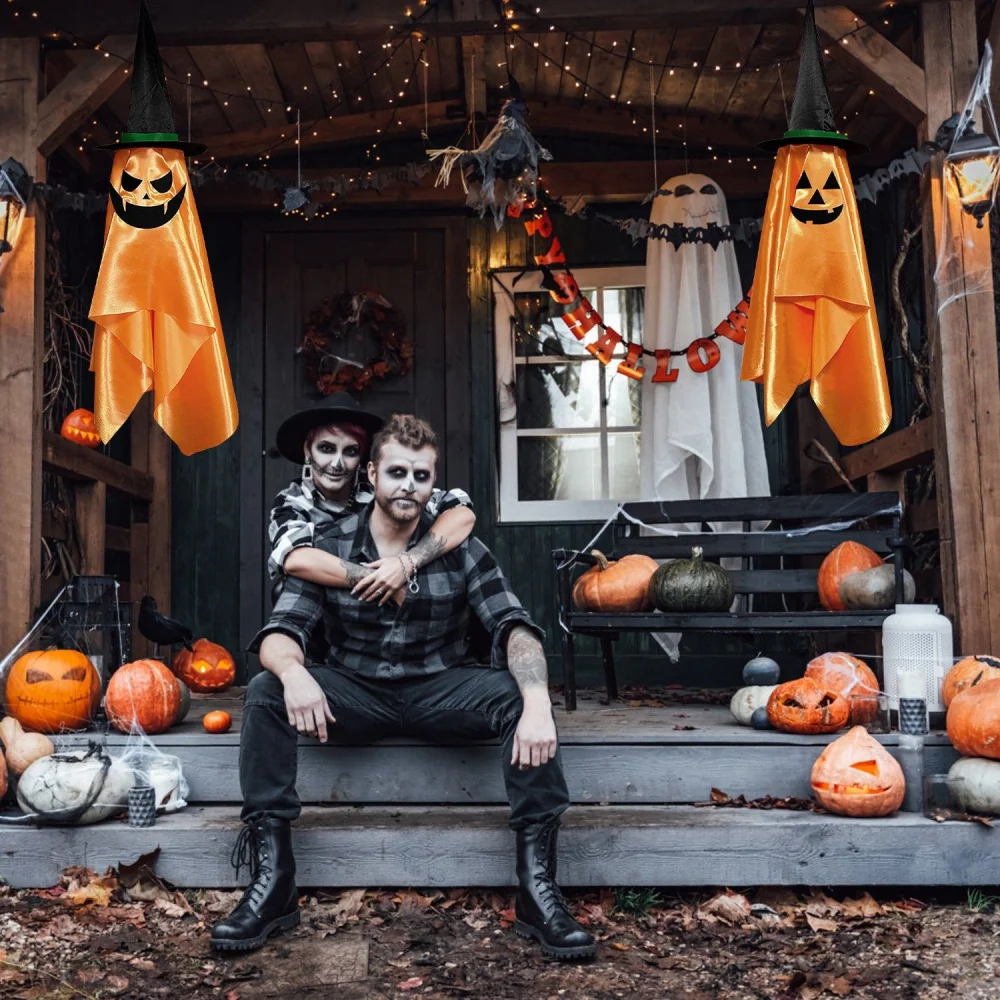 Autumn-themed Halloween scene featuring a couple sitting on a porch surrounded by carved pumpkins, spooky decorations, and festive lights, with two ghostly figures hanging above.