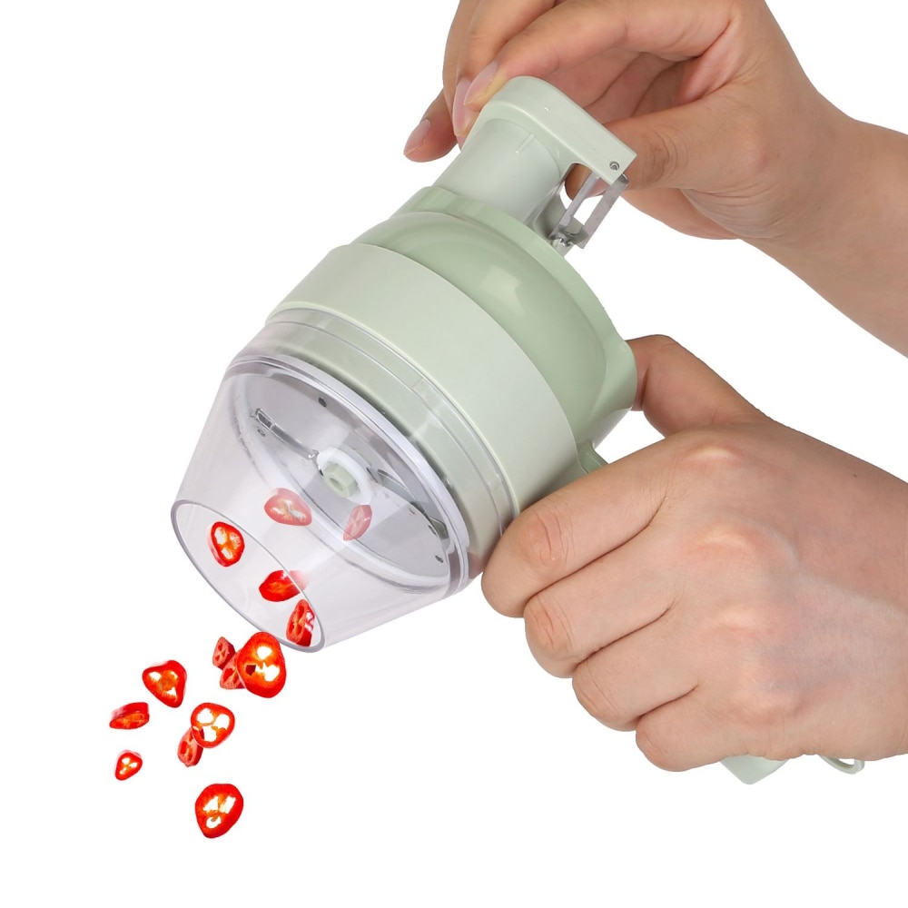 Handheld vegetable slicer showing sliced red chili peppers being dispensed from the clear container, with a pale green exterior and ergonomic grip for easy use in the kitchen.