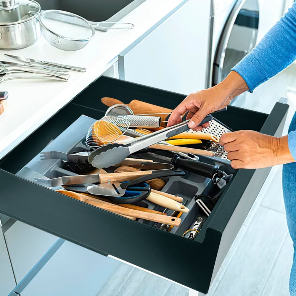 A person organizing a well-stocked kitchen drawer filled with various cooking utensils, including wooden spoons, tongs, and a grater, showcasing an efficient kitchen space.