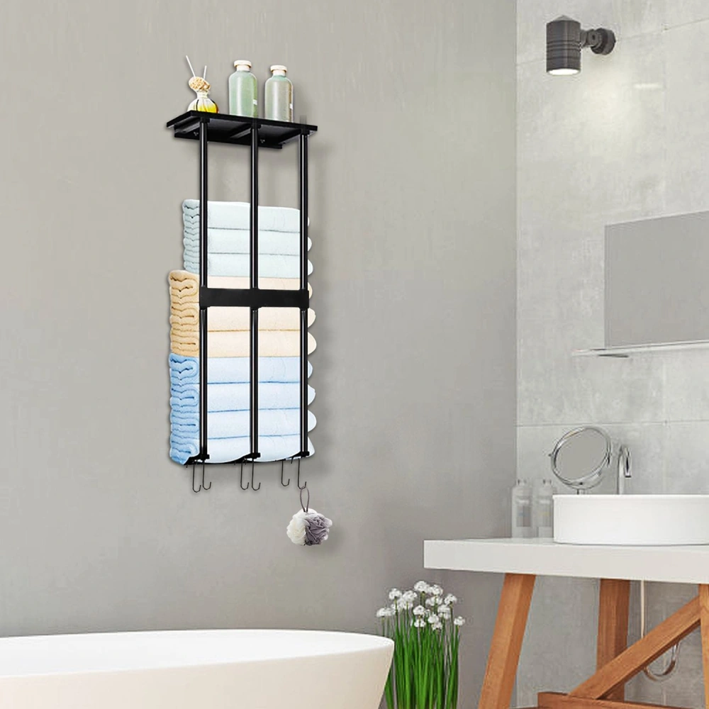Black metal towel rack organizer with neatly folded towels in pastel colors, decorative bottles on top, and hanging hooks, mounted on a light gray bathroom wall.