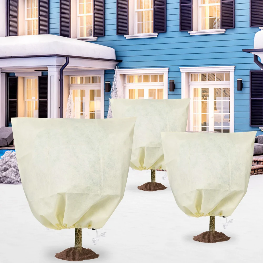 Protective fabric tree covers in front of a blue house, designed to shield young trees from harsh weather, featuring soft yellow material for insulation and secure base ties.