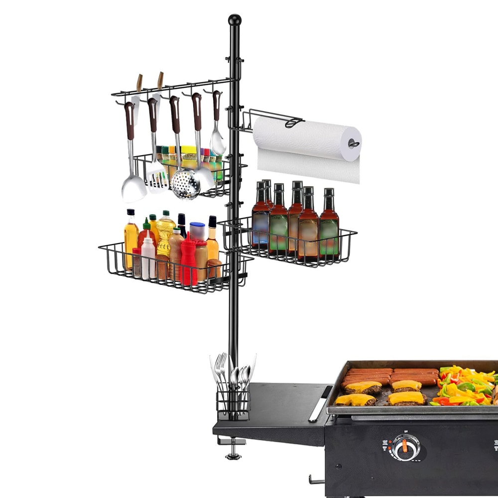Black grilling organizer with utensil holders, condiment and beverage storage, and paper towel holder next to a grill cooking burgers and vegetables.