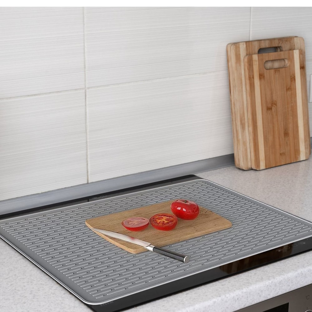 Silicone kitchen mat with a cutting board holding sliced tomatoes and a knife, set on a countertop with bamboo cutting boards in the background.