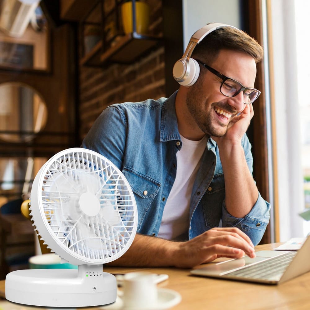 Portable white desktop fan providing a cool breeze to a focused individual working on a laptop in a cozy cafe setting.