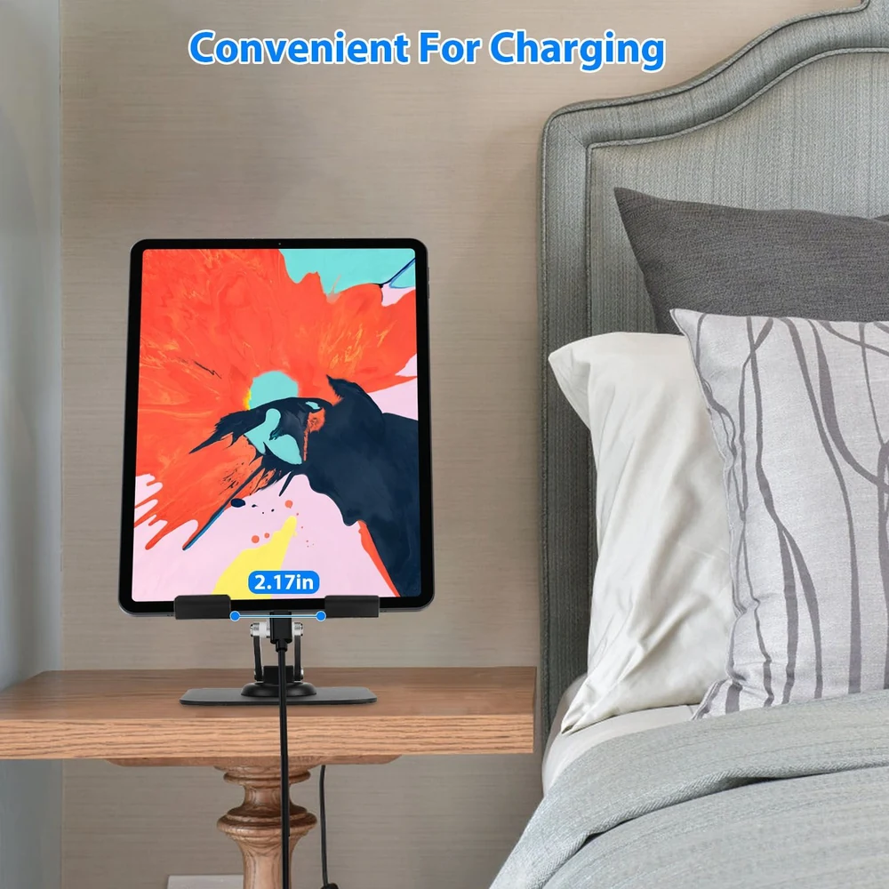 Tablet stand on a wooden bedside table with a charging cable, showcasing a colorful tablet screen, set against a cozy bedroom backdrop.