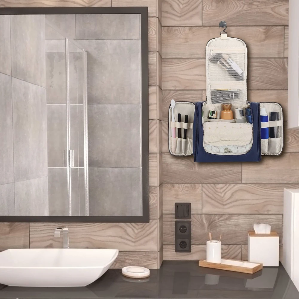 Hanging travel toiletry organizer with multiple compartments, mounted on a bathroom wall next to a modern sink and mirror, featuring various beauty products and accessories.