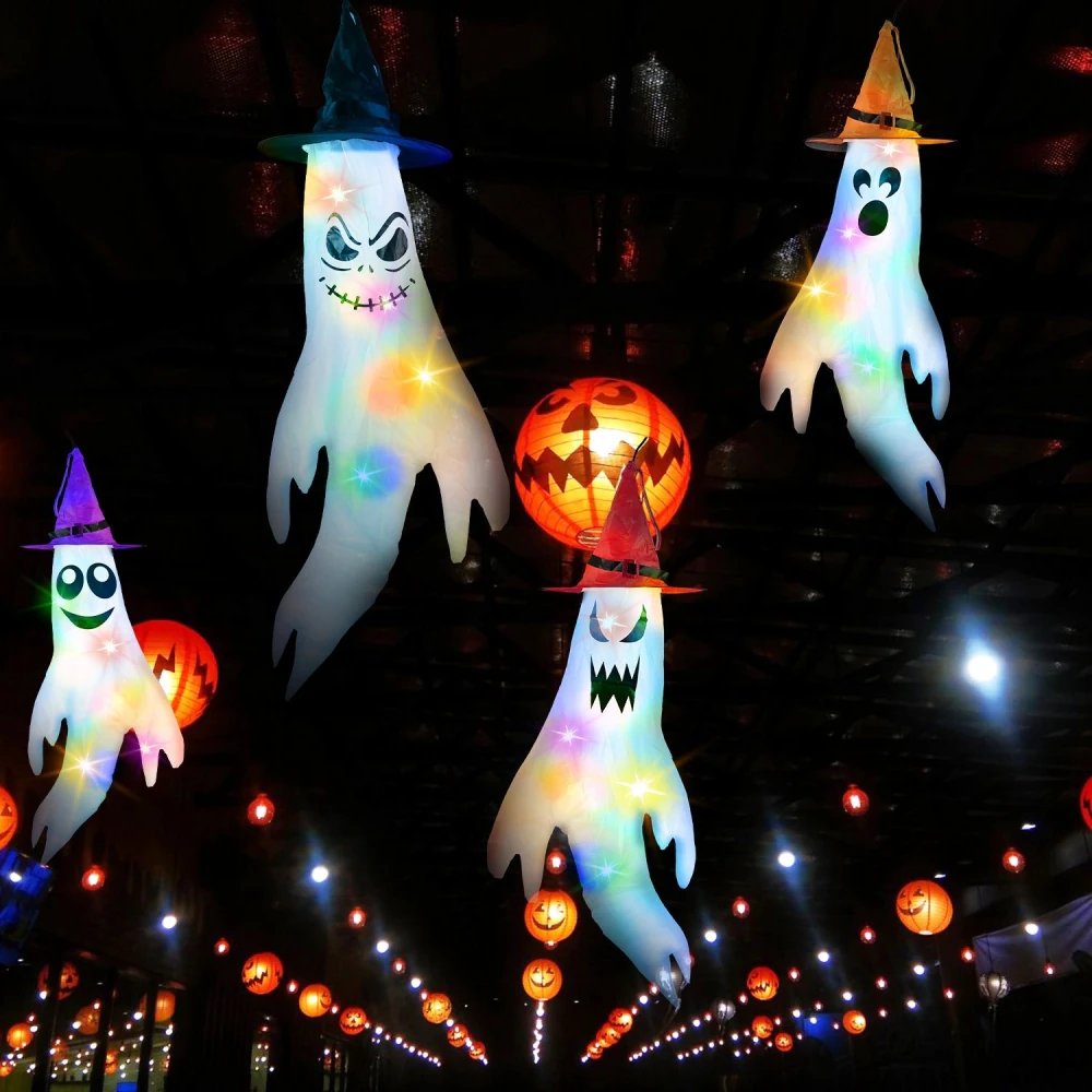 Colorful Halloween ghost decorations with witch hats, illuminated by glowing pumpkin lanterns in a festive setting.