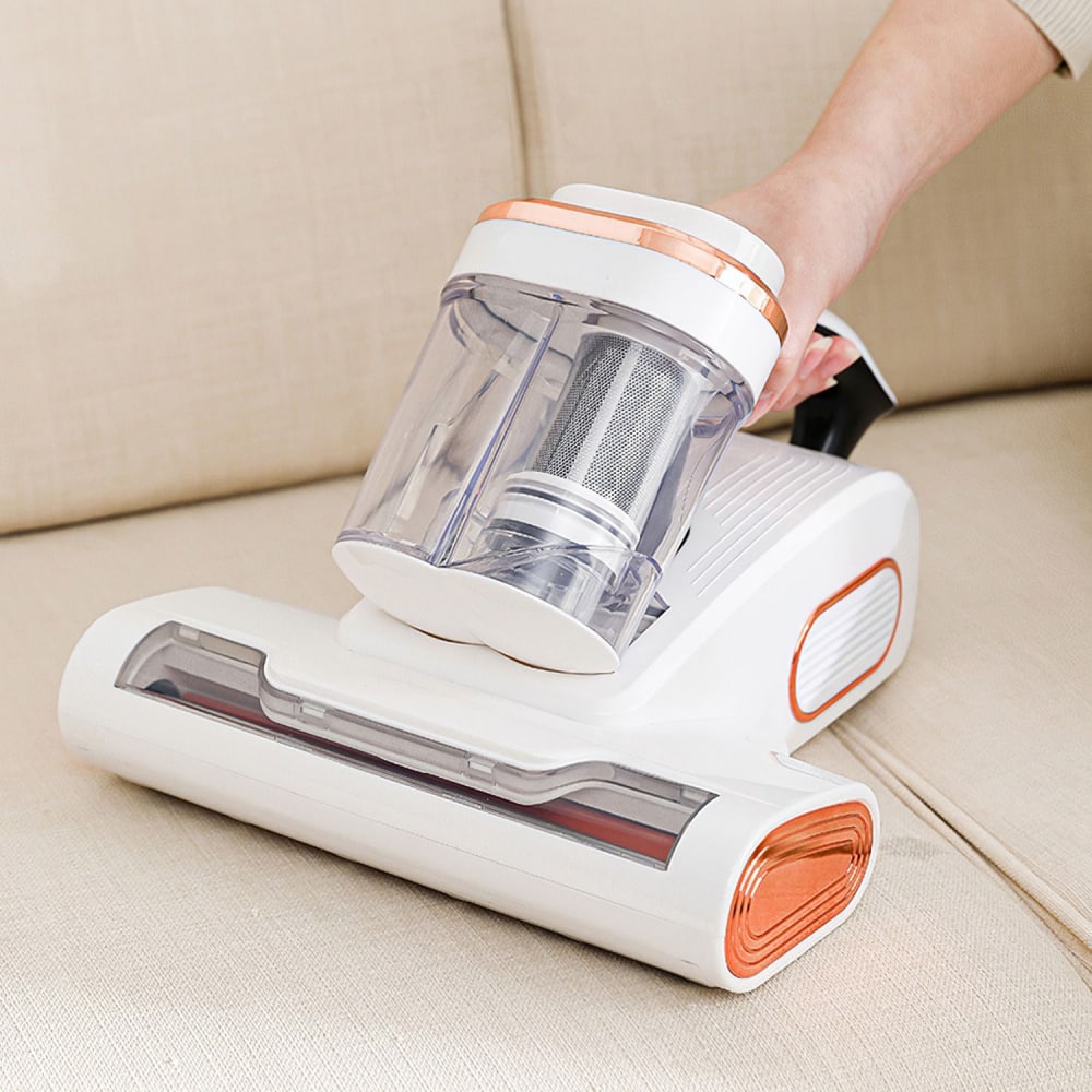 Handheld vacuum cleaner with a transparent dust container, designed for easy cleaning of upholstery, shown in use on a beige sofa.