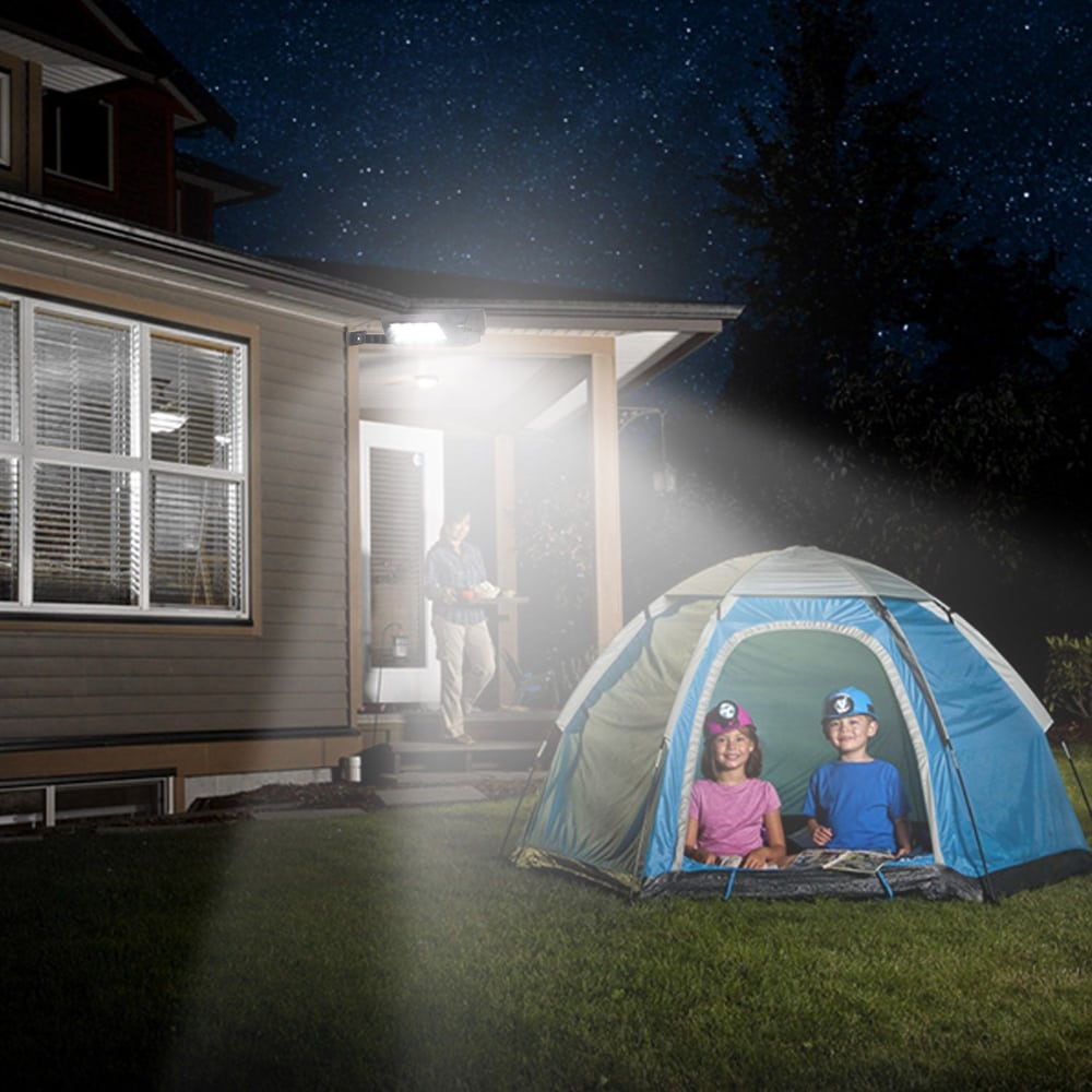 Children enjoying a camping night in a tent in the backyard under a starry sky, with a parent bringing supplies from the house.